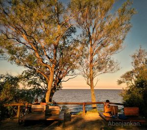 People sitting on bench by sea against sky during autumn