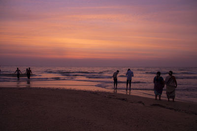 Silhouette people at beach against sky during sunset