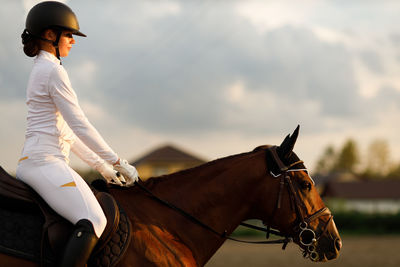 Side view of man riding horse on field against sky