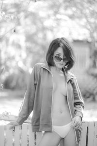 Portrait of seductive woman wearing leather jacket and sunglasses while standing by fence