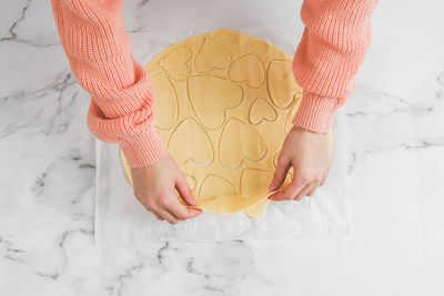 Hands of a young caucasian girl baker in the process of separating the raw dough with heart cutouts.