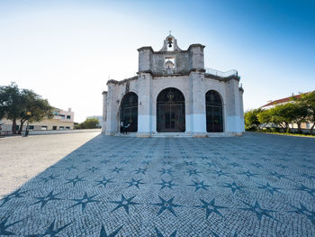 Octagonal backlit church casts long shadow on star decorated cobblestone square in lisbon