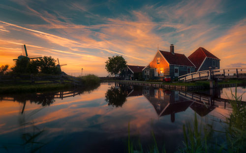 Scenic view of lake by buildings against sky during sunset