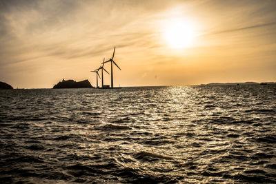 Silhouette of traditional windmill by sea against sky during sunset