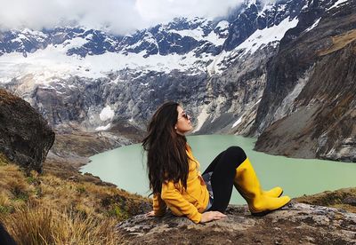 Young woman sitting on rock by snowcapped mountain