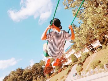 Low angle view of young woman swinging against sky