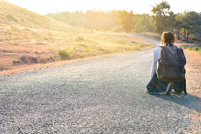Rear view of teenage girl carrying bag kneeling on road