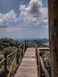 Wooden footbridge leading to sea against sky