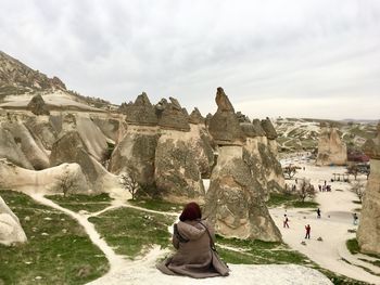 Rear view of woman sitting on rock against sky