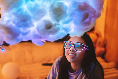 Smiling young woman looking at colorful cotton decoration in illuminated room