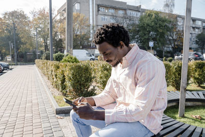 Young man using smart phone sitting on bench