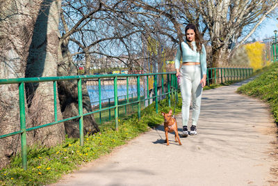 Young girl walking with her cute miniature pinscher by the lake.