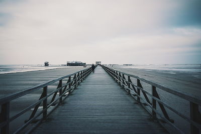 Pier at beach against cloudy sky at dusk