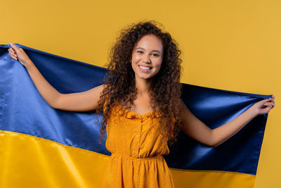 Portrait of young woman standing against yellow background