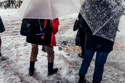 Rear view of people with umbrellas standing on snow covered field