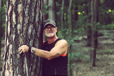 Portrait of a man standing and smiling by tree trunk in forest