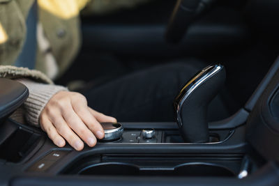 Young caucasian woman hand's turns the control wheel of a modern multimedia system in the car. 