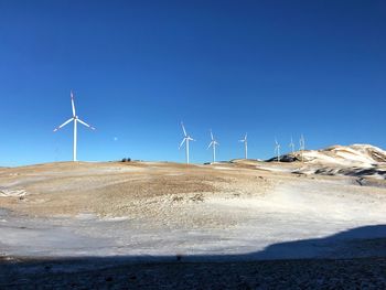 Wind turbines on land against clear blue sky