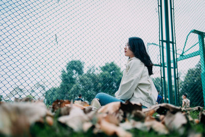 Surface level view of young woman sitting against chainlink fence