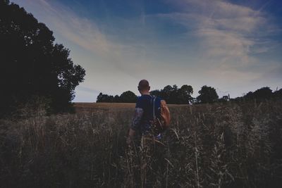 Side view of man with backpack standing on land against sky