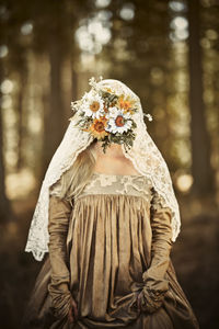 Bide with flower covering face standing in forest