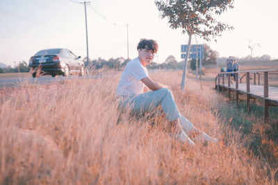 Side view of young man sitting on field against sky