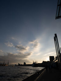 Silhouette buildings by sea against sky during sunset