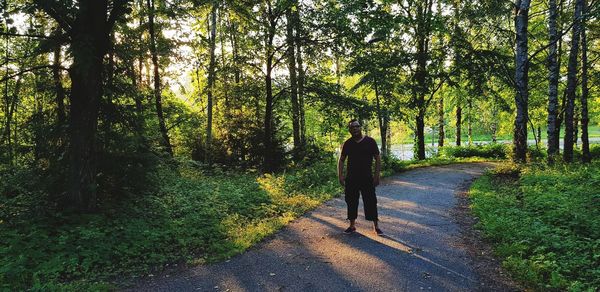 Rear view of woman walking on road amidst trees in forest