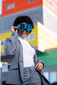 A cool young african american lady with curly hair and ski goggles in an area of modern buildings