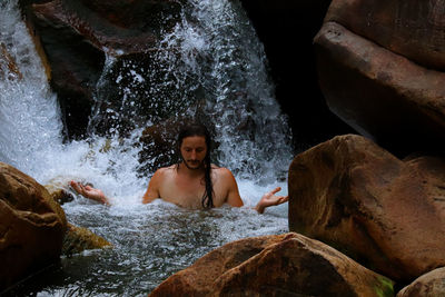 Full length of shirtless man splashing water in rock