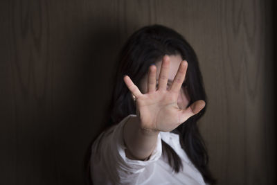 Young woman showing hand while standing against wooden wall