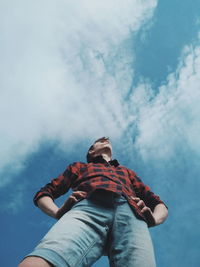 Low angle view of teenage boy standing against blue sky