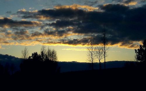 Silhouette trees on landscape against dramatic sky