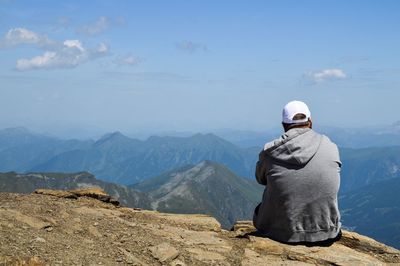 Rear view of man sitting on mountain against sky