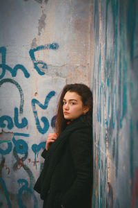 Portrait of woman standing against graffiti wall