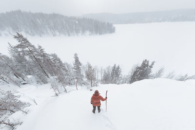 A man with a staff stands on a snow-covered hill and admires the winter view. wild remote area