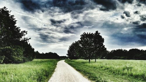 Road passing through field against cloudy sky