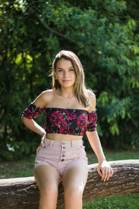 Portrait of teenage girl sitting on tree trunk against plants in park