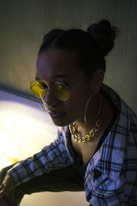 Portrait of young woman wearing sunglasses against wall