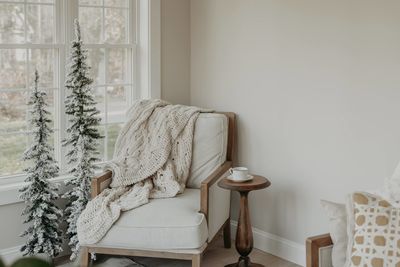 Empty armchair with cable knit blanket and decorative tree in white room