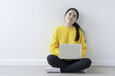 Portrait of woman using phone while sitting on wall