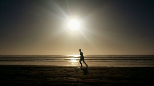 Silhouette man standing on beach against sky during sunset