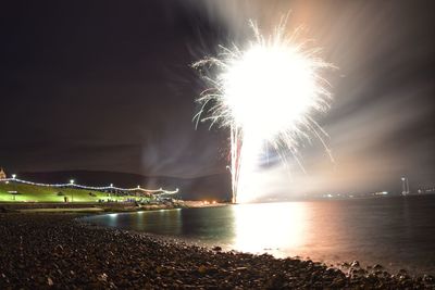 Firework display over sea against sky at night