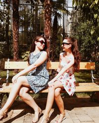 Beautiful women sitting on bench against trees