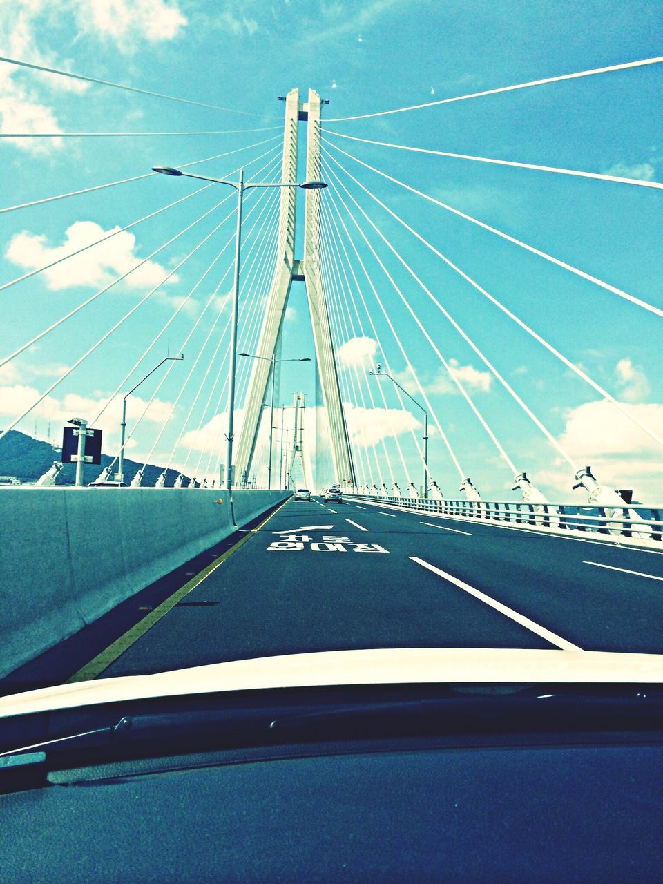 transportation, connection, bridge - man made structure, sky, blue, engineering, suspension bridge, road, the way forward, mode of transport, low angle view, travel, road marking, diminishing perspective, built structure, cable-stayed bridge, car, cloud - sky, vanishing point, day