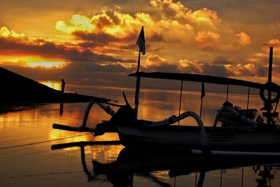 Silhouette boat moored on lake against sky during sunset