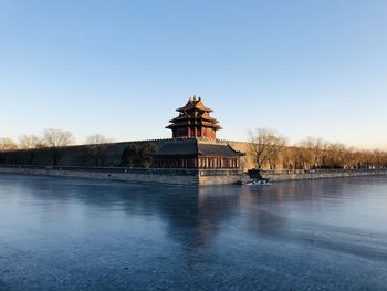 Building by lake against clear blue sky