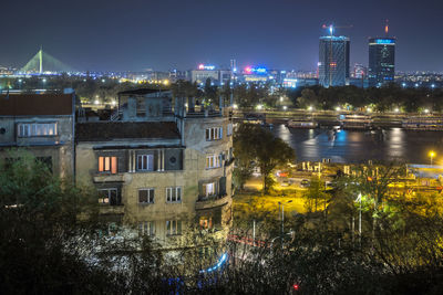 Illuminated buildings by river against sky in city at night