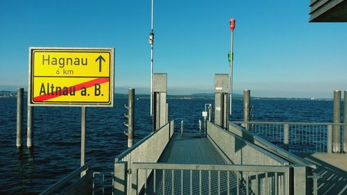 Information sign by sea against clear blue sky