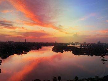 Scenic view of river by buildings against sky during sunset